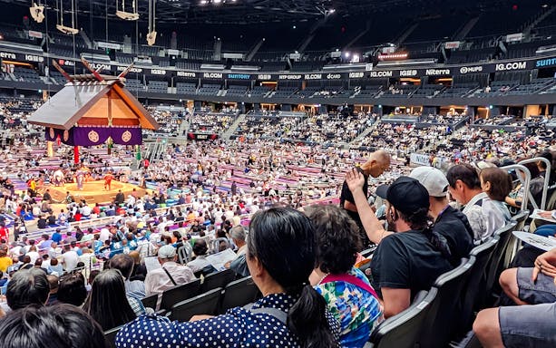 Spectators watching a sumo match at the Nagoya Grand Sumo Tournament in a crowded arena.