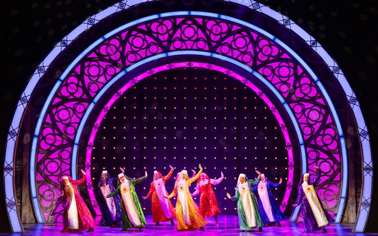 Performers in colorful costumes dancing on stage during a Sister Act musical scene.