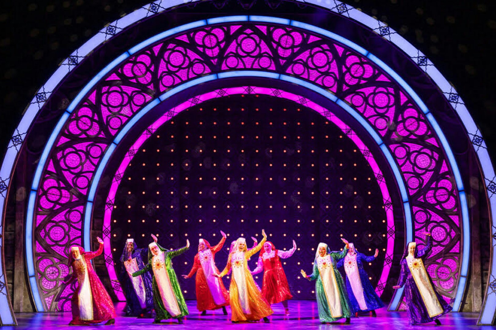 Performers in colorful costumes dancing on stage during a Sister Act musical scene.
