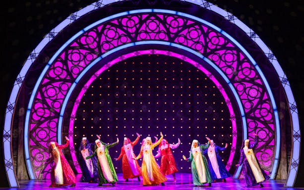 Performers in colorful costumes dancing on stage during a Sister Act musical scene.