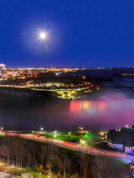 Niagara Falls illuminated at night with city lights in the background, Canada.