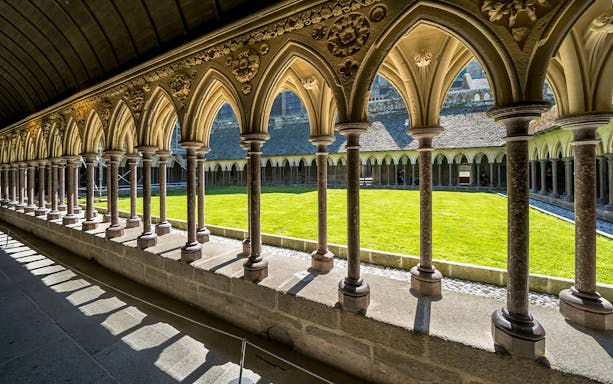 Cloister arches at Mont St. Michel with view of the courtyard lawn.