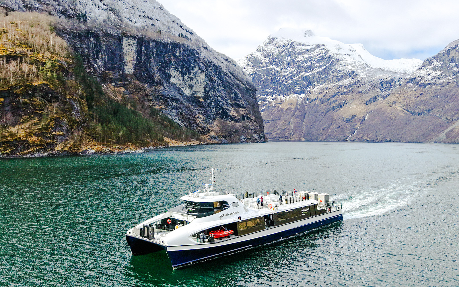 Cruise ship sailing through Geirangerfjord with snow-capped mountains in Norway.