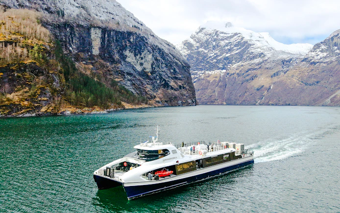 Cruise ship sailing through Geirangerfjord with snow-capped mountains in Norway.