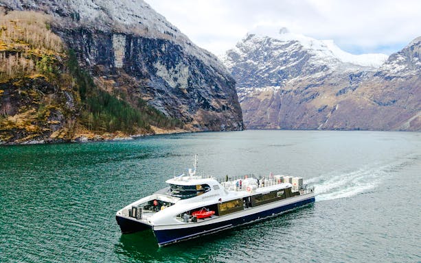 Cruise ship sailing through Geirangerfjord with snow-capped mountains in Norway.