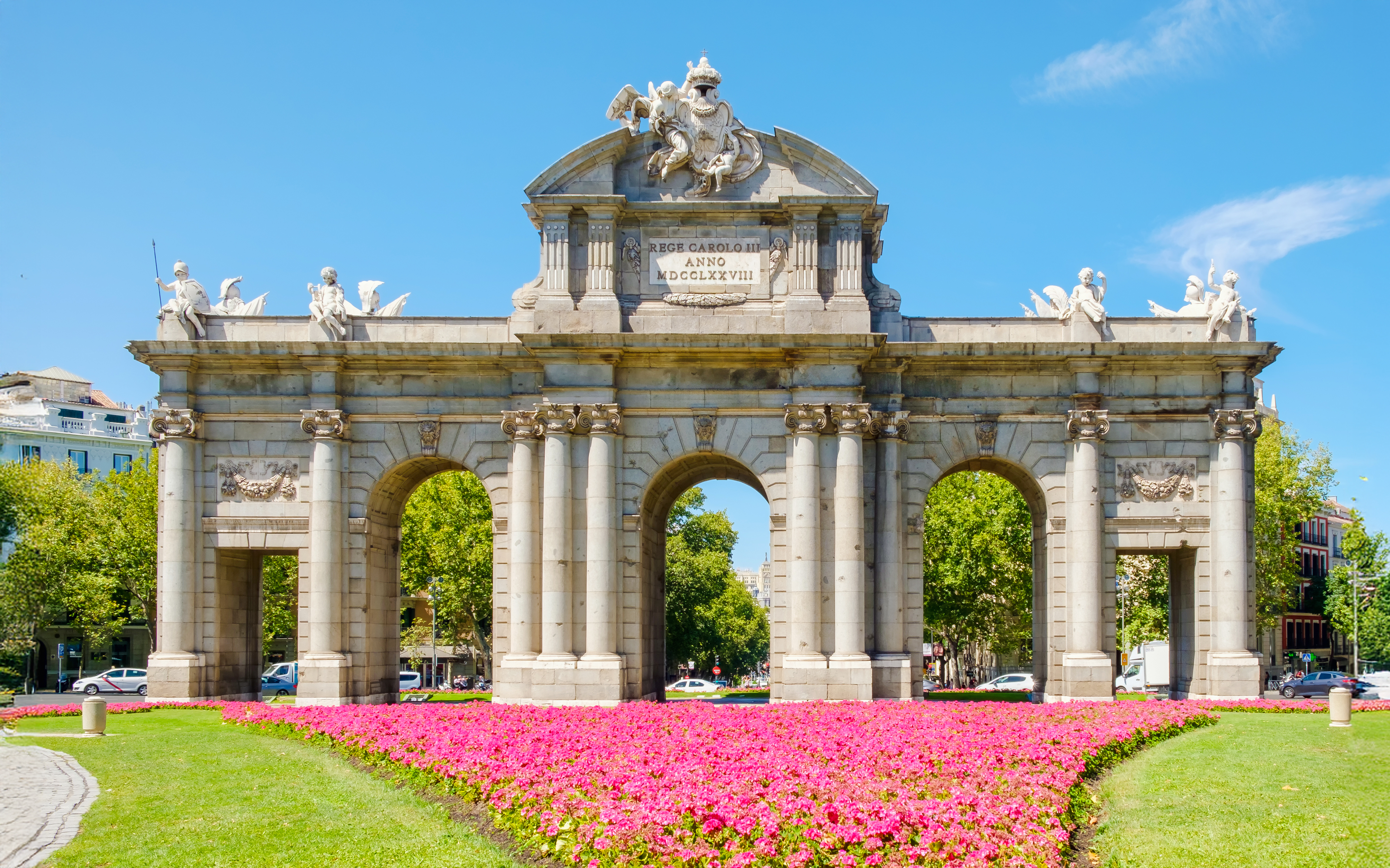 Puerta de Alcala in Madrid with vibrant pink flowers in the foreground.