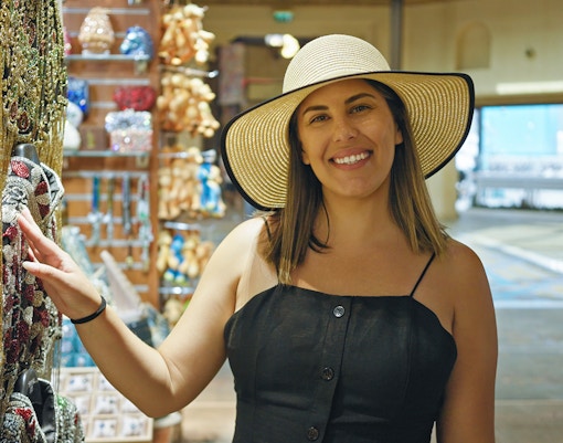 Woman shopping for souvenirs in a local market, wearing a sun hat.