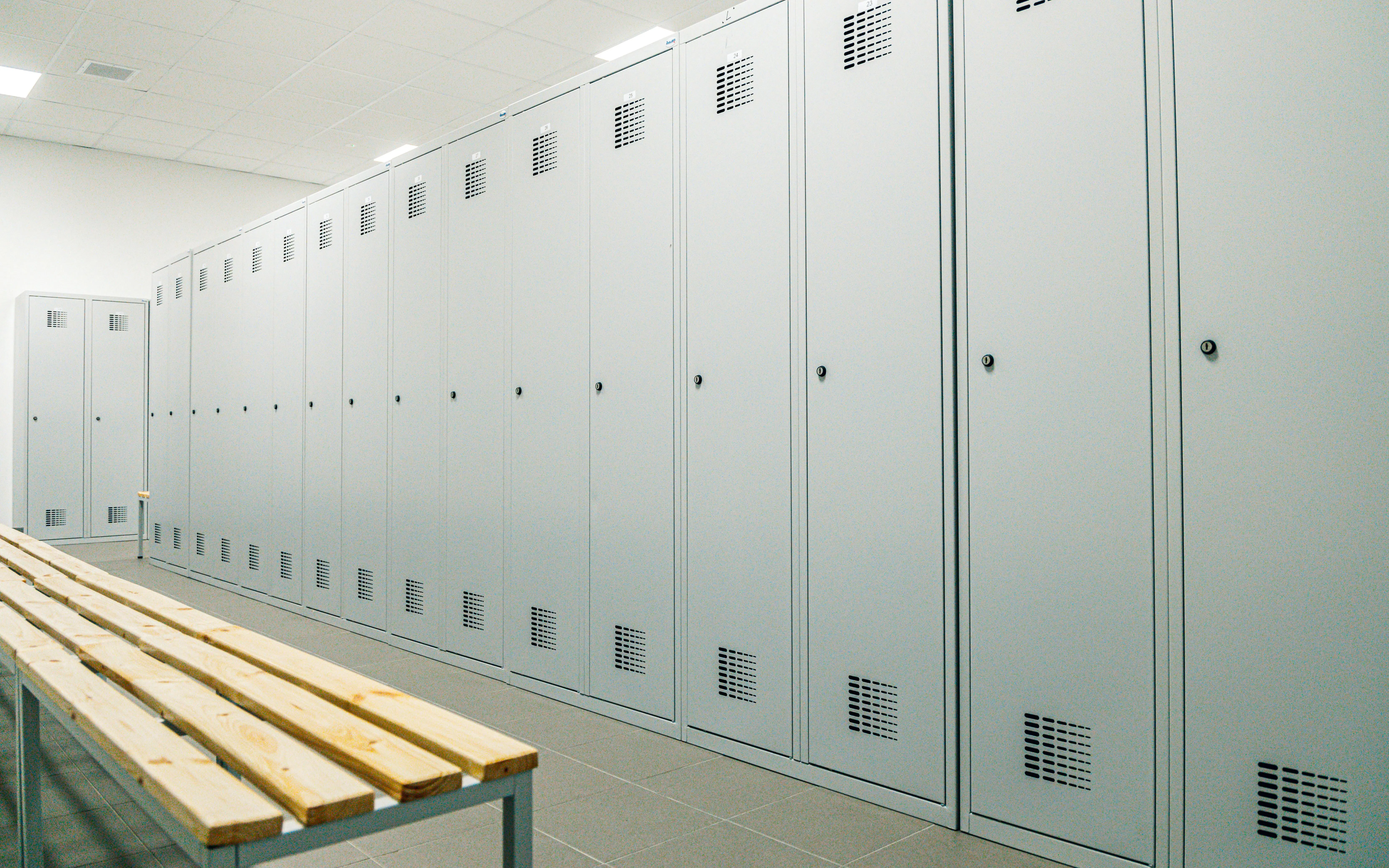 Locker room with rows of gray lockers and a wooden bench.
