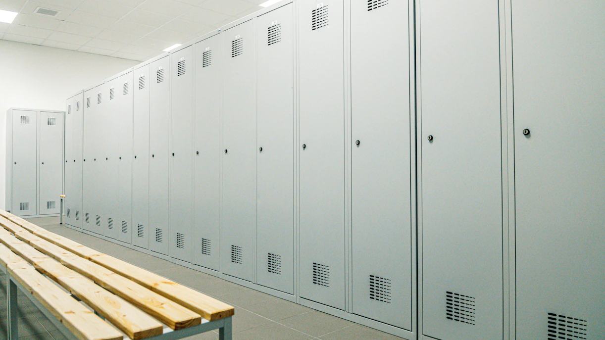 Locker room with rows of gray lockers and a wooden bench.