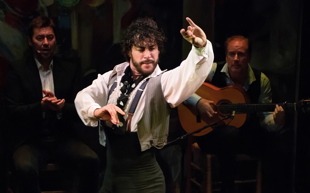 Flamenco dancer performing at Teatro Flamenco Triana with guitarist in background.