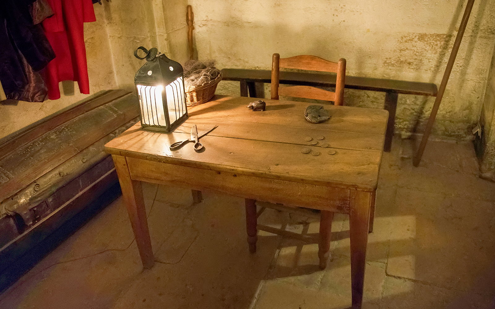 Wooden table with lantern, coins, and scissors in a historic palace room.