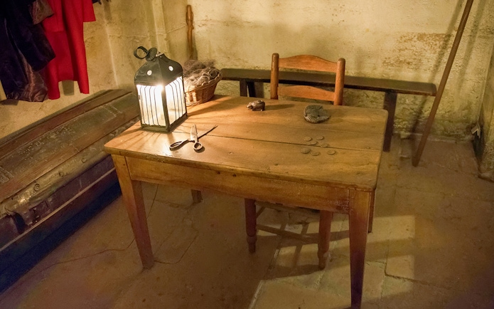 Wooden table with lantern, coins, and scissors in a historic palace room.