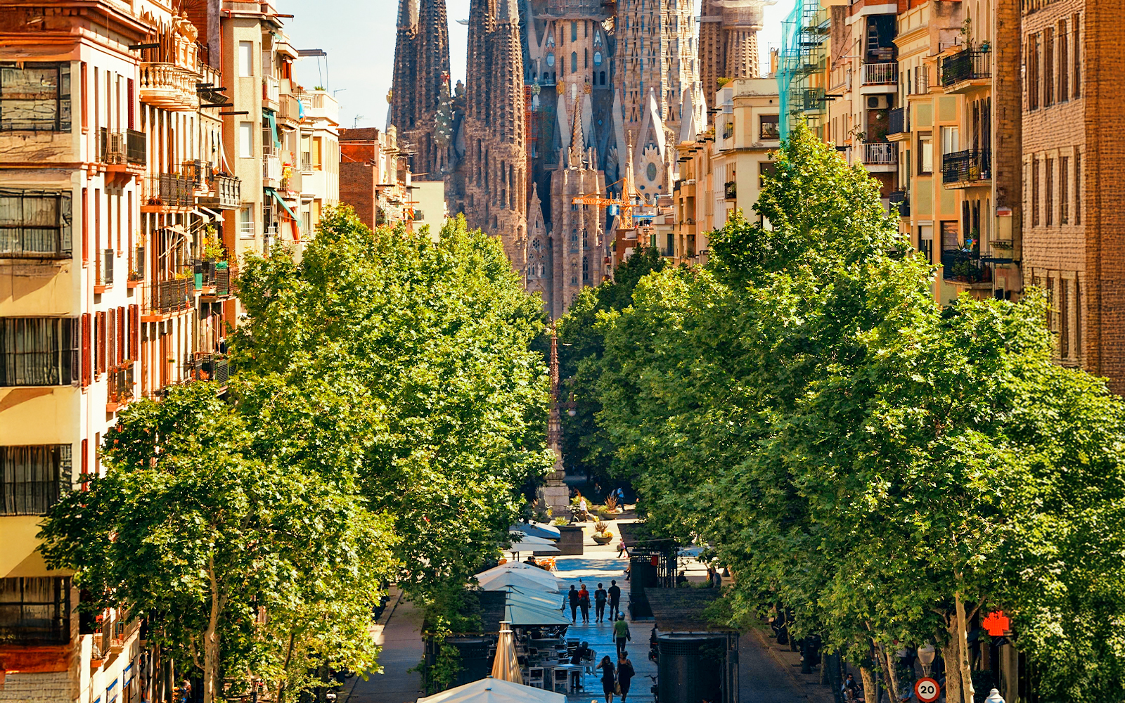 Sagrada Familia viewed from Plaça de la Sagrada Família, framed by trees and buildings.