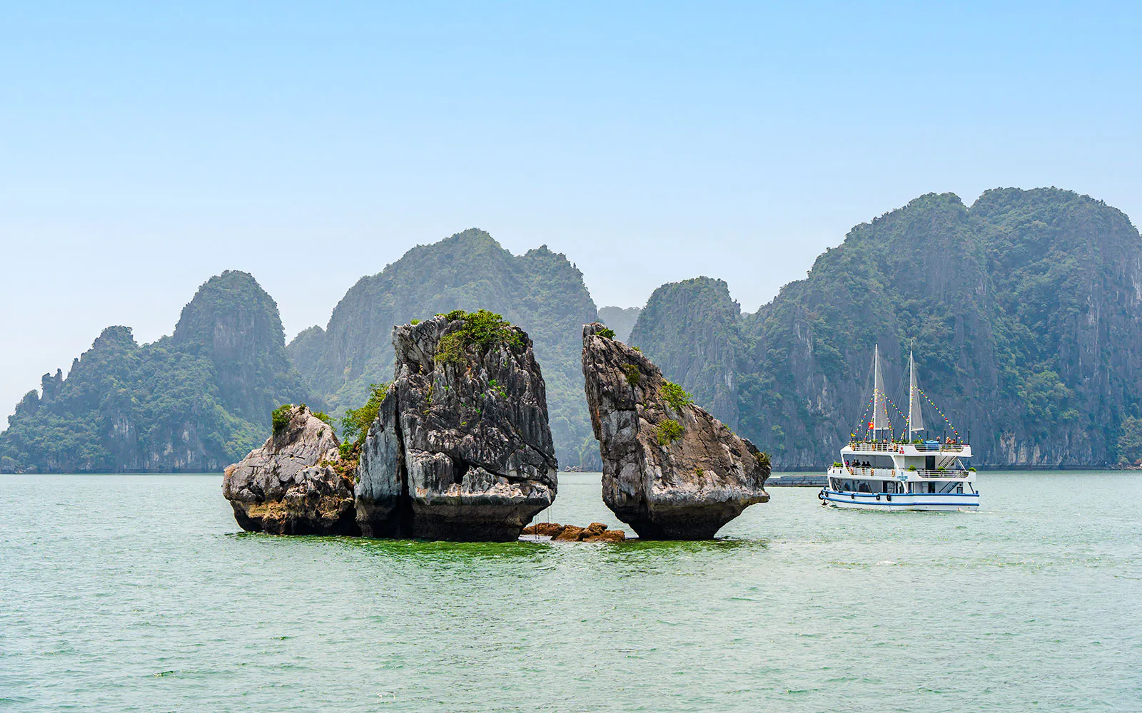 Fighting Cocks Islets in Ha Long Bay, Vietnam with a tour boat nearby.