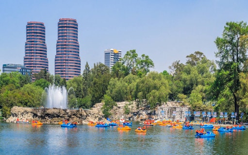 Paddle boats on a lake in Chapultepec Park with city skyline in the background.