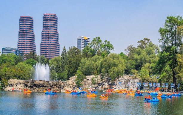 Paddle boats on a lake in Chapultepec Park with city skyline in the background.