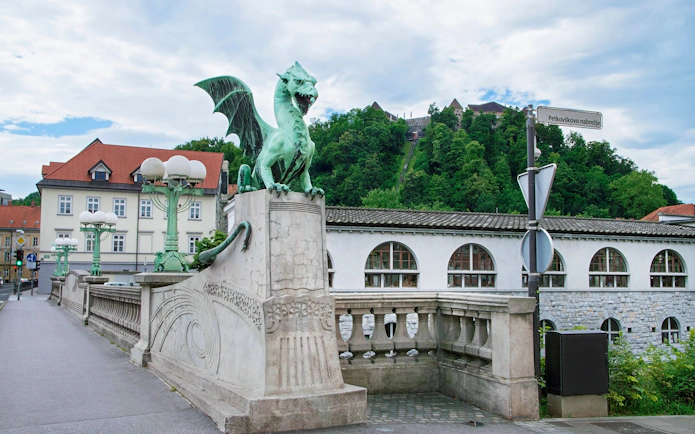 Dragon Bridge statue with Ljubljana Castle in the background, Slovenia.