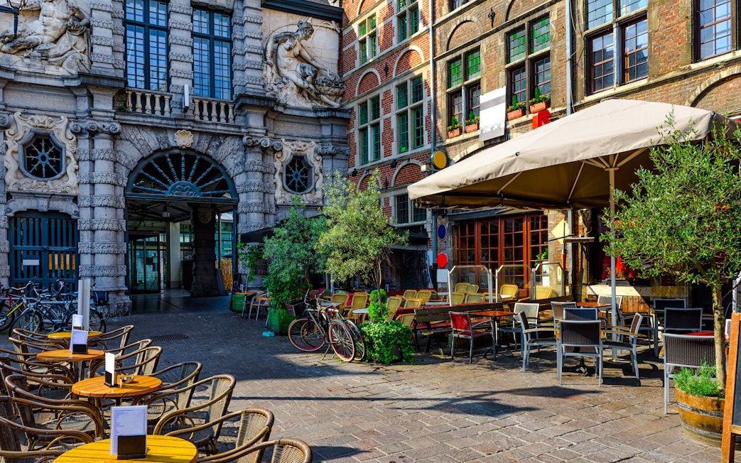 Outdoor café with tables and chairs in the historic city center of Ghent, Belgium, on a sunny day.