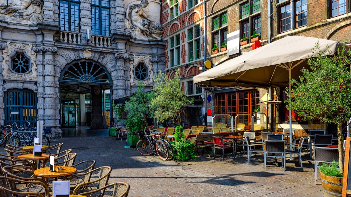 Outdoor café with tables and chairs in the historic city center of Ghent, Belgium, on a sunny day.