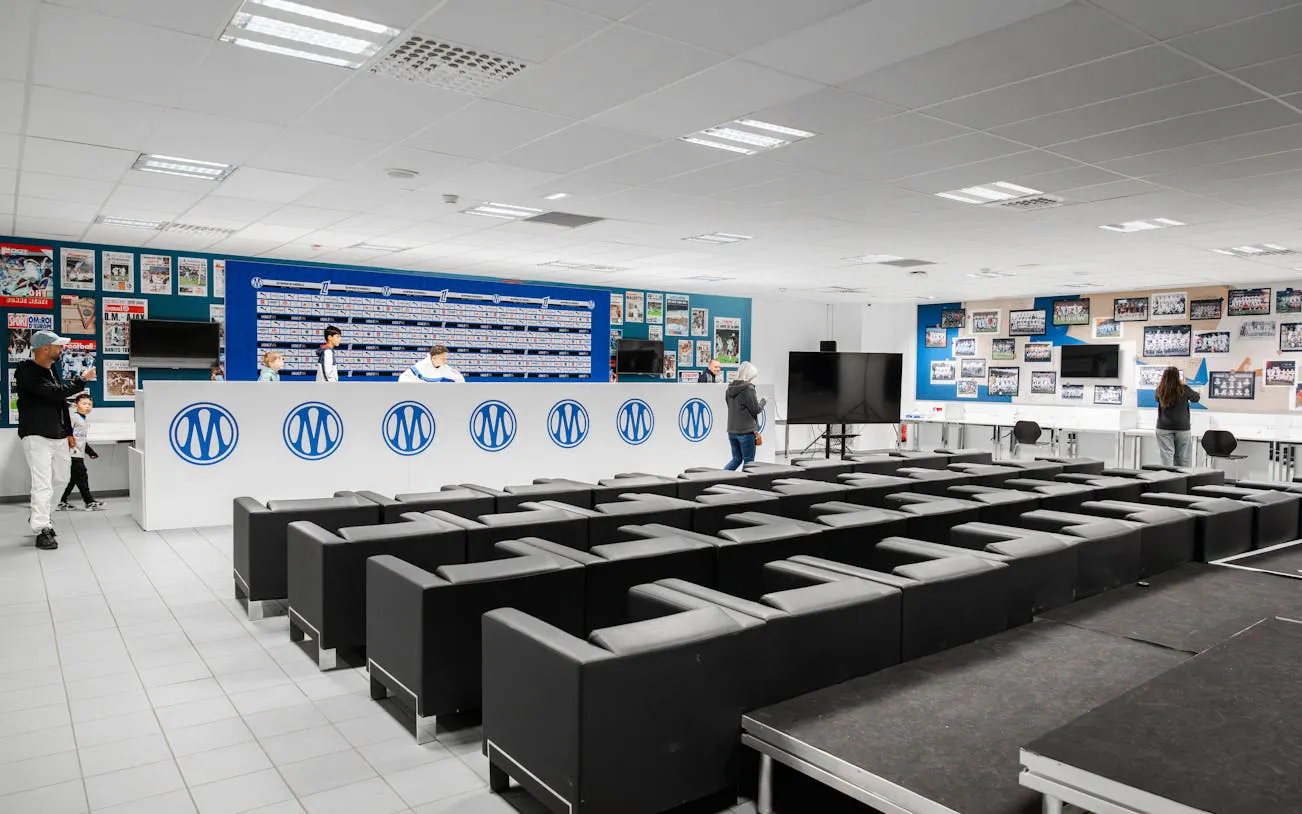 Press room at CEPAC Vélodrome during OM guided tour, featuring seating and display wall.