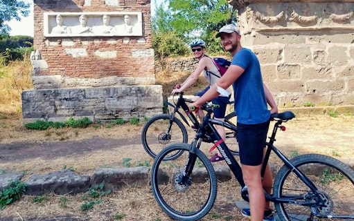 Cyclists on E-Bike Guided Tour of Appia Antica near ancient Roman ruins.