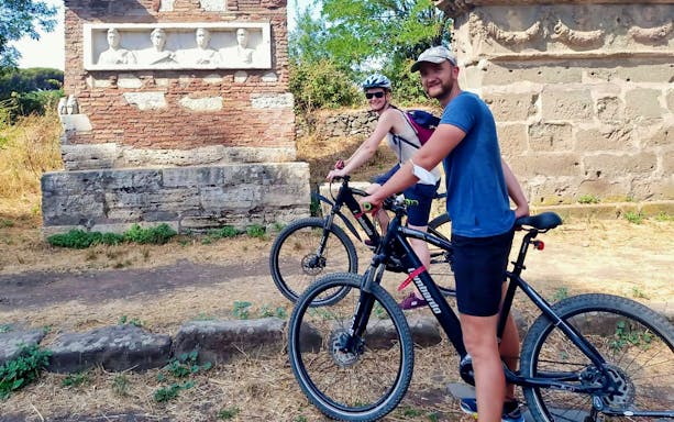 Cyclists on E-Bike Guided Tour of Appia Antica near ancient Roman ruins.