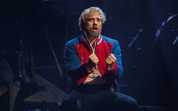Performer in Les Misérables musical scene, wearing a red and blue costume.