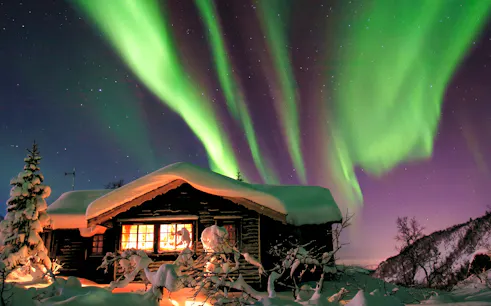 Northern Lights over snowy cabin at Chena Hot Springs, Alaska.