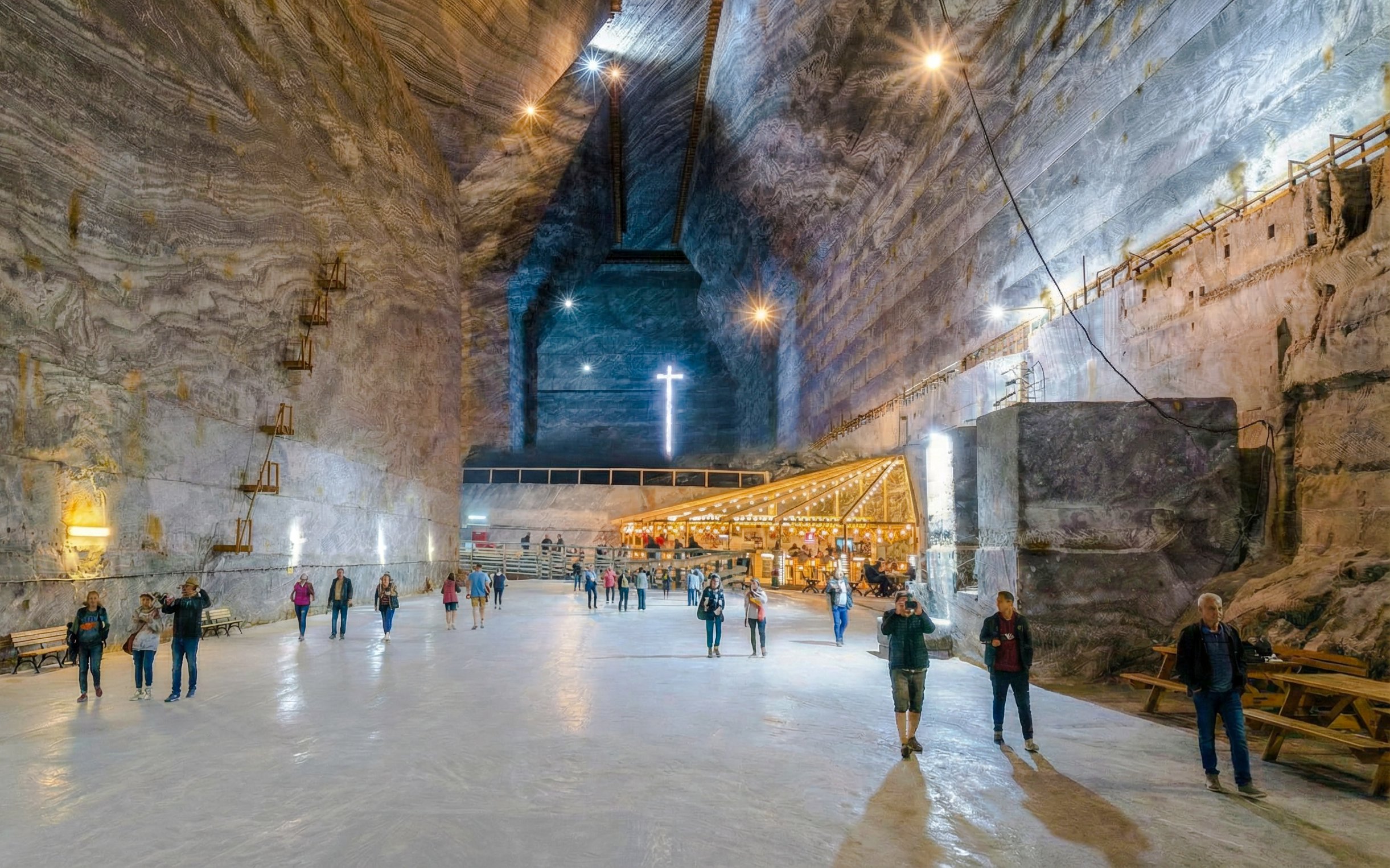 Visitors walking inside Slanic Salt Mine, Romania, with illuminated cross and seating area.