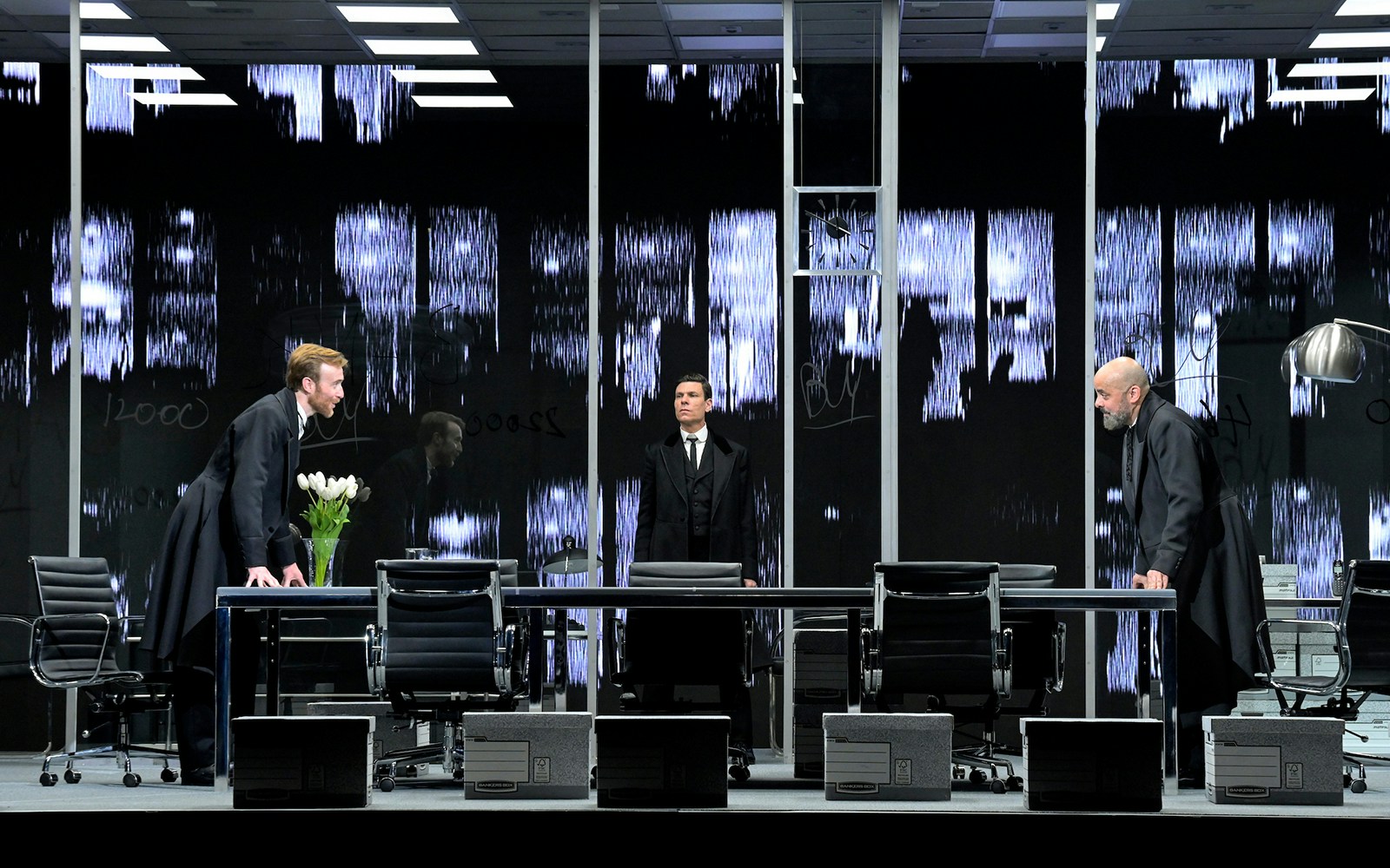 Three actors in a modern office setting during a scene from The Lehman Trilogy.