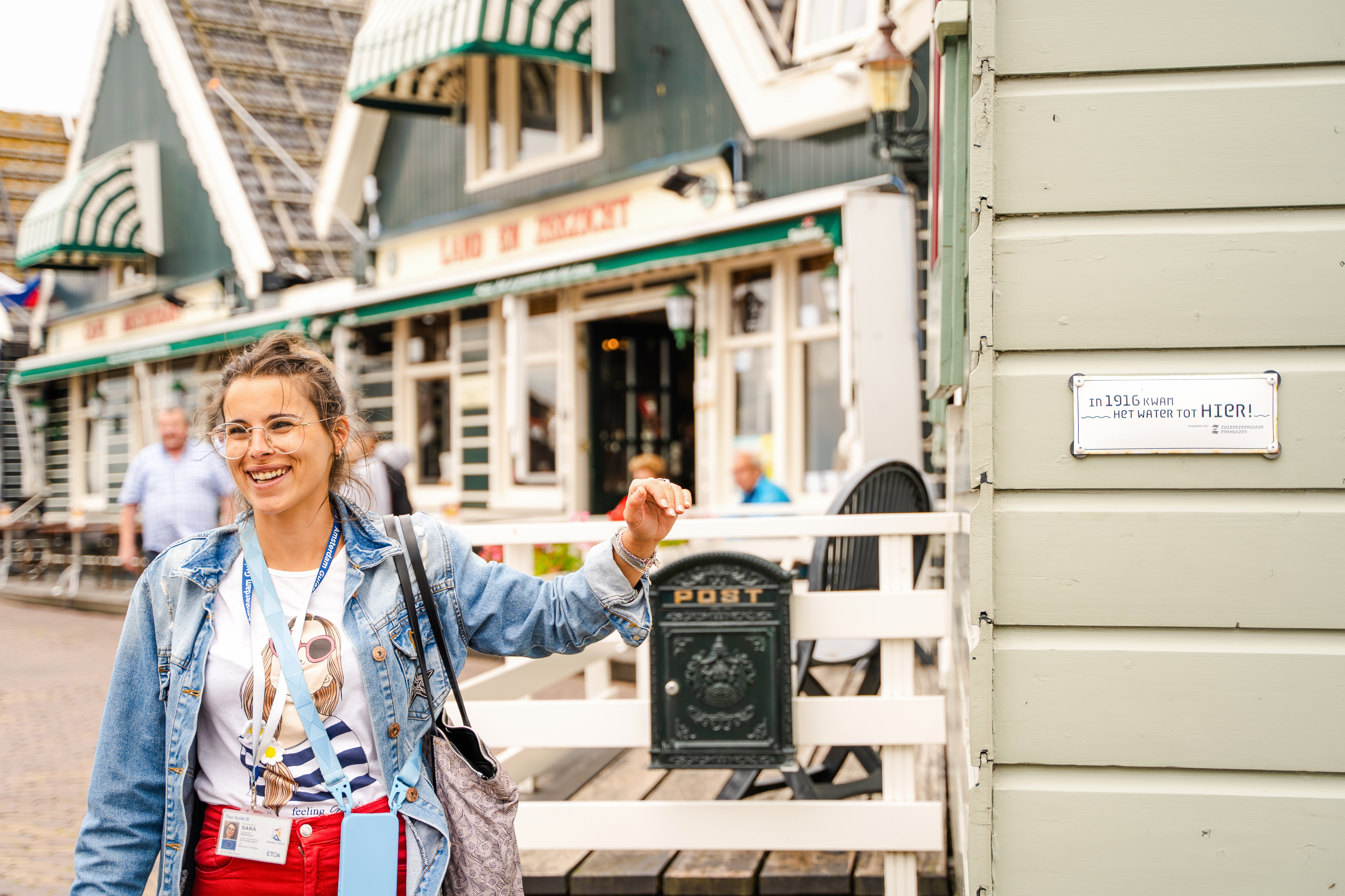 Tour guide in Volendam near historic building with flood marker sign.
