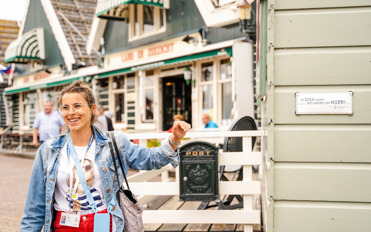 Tour guide in Volendam near historic building with flood marker sign.