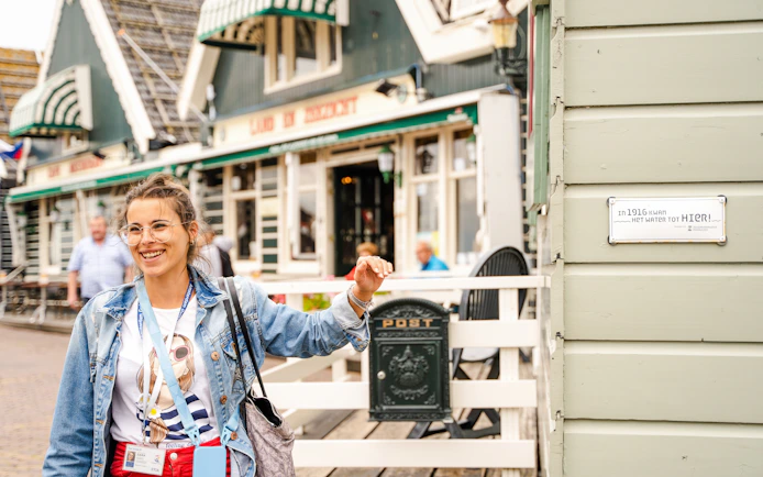 Tour guide in Volendam near historic building with flood marker sign.