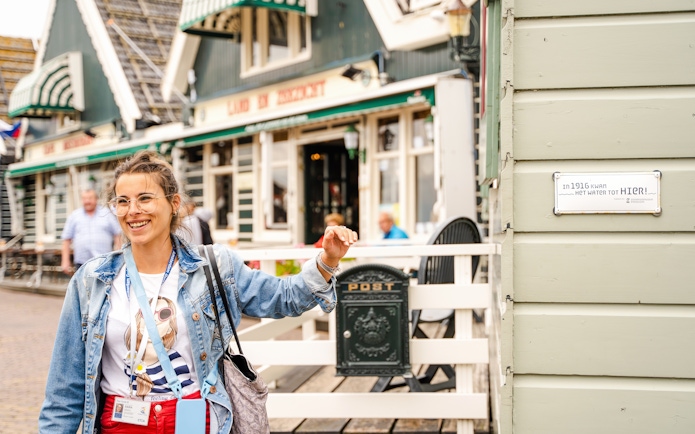 Tour guide in Volendam near historic building with flood marker sign.