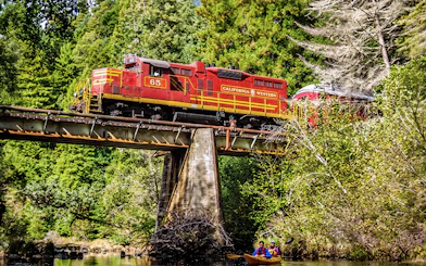 California Western train crossing a bridge with kayakers below on the Willits' Historic Wolf Tree Turn tour in San Francisco.