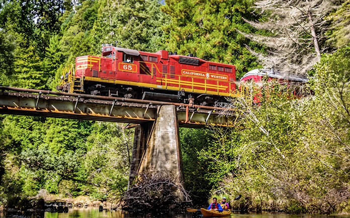 California Western train crossing a bridge with kayakers below on the Willits' Historic Wolf Tree Turn tour in San Francisco.