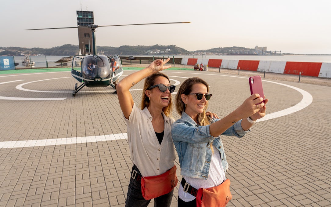 Helicopter on Lisbon helipad with two women taking a selfie before flight.