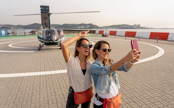 Helicopter on Lisbon helipad with two women taking a selfie before flight.