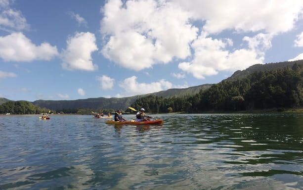 Kayakers paddling on Furnas Lake with lush hills in the background.
