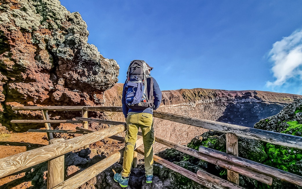 Hiker on Mount Vesuvius trail with view of crater, Italy.