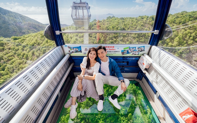 Couple enjoying a ride in a crystal cabin cable car with scenic views of lush greenery below.
