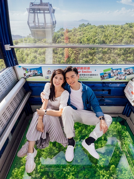 Couple enjoying a ride in a crystal cabin cable car with scenic views of lush greenery below.