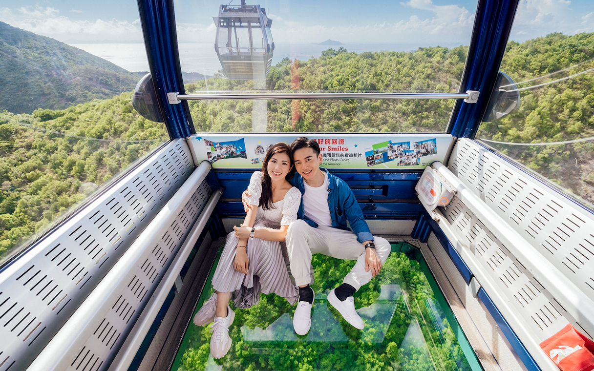 Couple enjoying a ride in a crystal cabin cable car with scenic views of lush greenery below.
