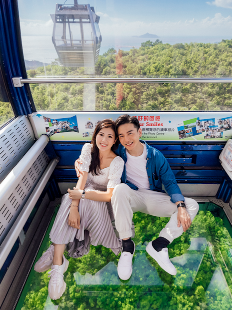 Couple enjoying a ride in a crystal cabin cable car with scenic views of lush greenery below.