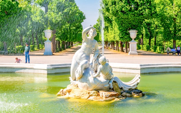 Fountain sculpture in Schönbrunn Palace gardens, Vienna, with lush greenery and visitors nearby.