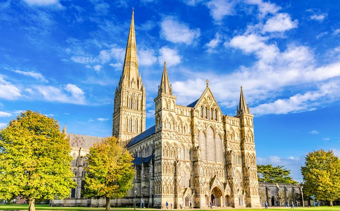 Salisbury Cathedral with its spire and Gothic architecture under a blue sky.
