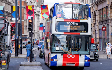 Toot bus navigating a busy street in London with colorful banners overhead.