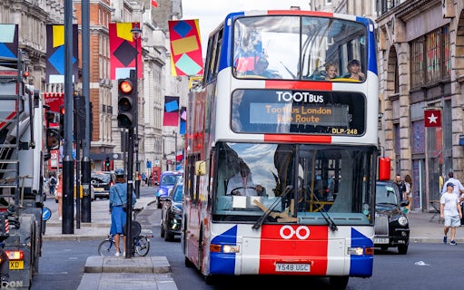 Toot bus navigating a busy street in London with colorful banners overhead.