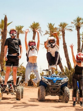 Group jumping in front of quad bikes in Palmeraie desert during sunset tour.