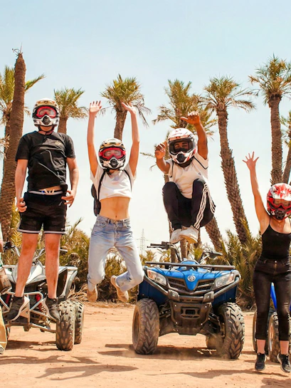 Group jumping in front of quad bikes in Palmeraie desert during sunset tour.